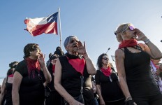 Feminist activists with a Chilean flag take part in a choreographed performance against gender violence, patriarchy and denounce an oppressive state, outside the national stadium in Santiago on December 04, 2019. 