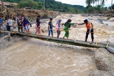 Work together: A police officer helps residents cross a makeshift emergency bridge over the Cidurian River in Bogor, West Java, 
on Friday. Antara/Arif Firmansyah