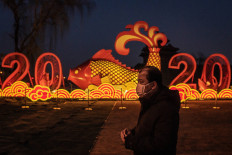 A man wears a protective facemask to help stop the spread of a deadly SARS-like virus which originated in the central city of Wuhan, as he walks on the outskirts of the Forbidden City and a New Year instalation displaying a fish and the number 2020 in Beijing on January 25, 2020. 