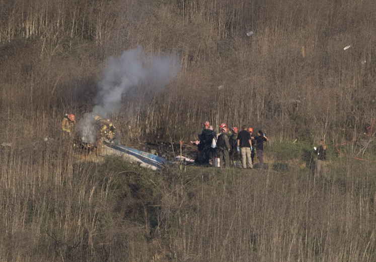Los Angeles County Fire Department firefighters and coroner staff check the wreckage at the scene of a helicopter crash in Calabasas on January 26, 2020. - Nine people were killed in the helicopter crash which claimed the life of NBA star Kobe Bryant and his 13-year-old daughter, Gianna, Los Angeles officials confirmed on Sunday. Los Angeles County Sheriff Alex Villanueva said eight passengers and the pilot of the aircraft died in the accident. The helicopter crashed in foggy weather in the Los Angeles suburb of Calabasas. Authorities said firefighters received a call shortly at 9:47 am about the crash, which caused a brush fire on a hillside. / (Photo by Mark RALSTON / AFP)