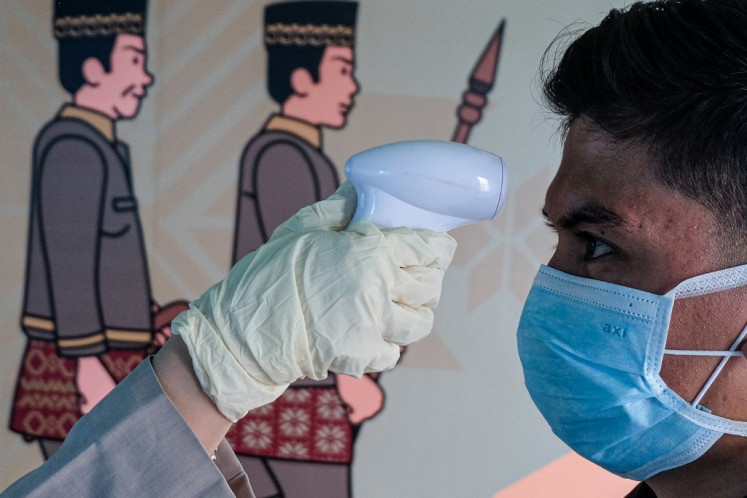 A person checks the temperature of a passenger (R) wearing a facemask to help stop the spread of a deadly virus which began in the Chinese city of Wuhan, as he arrives at the Sultan Mahmud Badaruddin II International airport in Palembang on January 26, 2020. (Photo by ABDUL QODIR / AFP)