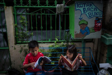 Two children of the Jatipulo literacy kampung read books, seated on a bench beneath a decorated book-sharing box. JP/Afriadi Hikmal
