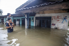 A resident wades through water while carrying a child during a flood in Cilangkap, East Jakarta, on Tuesday. Heavy rains since Monday morning have caused parts of the capital to flood.