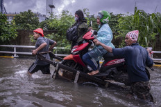 Novel commute: Two men use a cart to carry a motorcycle, its ride-hailing driver and her passenger through floodwaters on the morning of Feb. 25 in Grogol, Jakarta. 