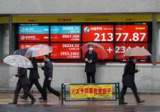 Passersby wearing protective face masks, following an outbreak of the coronavirus, walk past in front of an electric screen displaying Nikkei share average outside a brokerage in Tokyo, Japan March 2, 2020.   REUTERS/Issei Kato