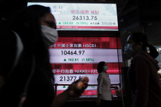 People wear protective masks as they walk past a panel displaying the Hang Seng Index during morning trading following the outbreak of COVID-19 in Hong Kong, China, on March 2, 2020.
