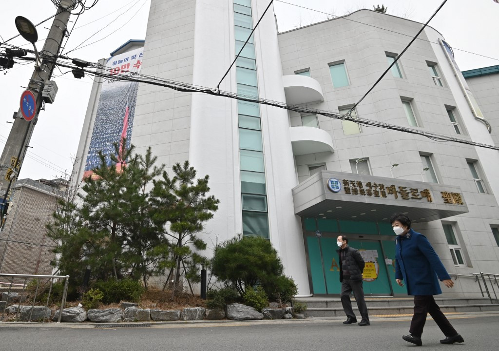 People wearing face masks walk past a branch of the Shincheonji Church of Jesus, which is temporarily closed by the government to help prevent the spread of the COVID-19 coronavirus, in Seoul on March 1, 2020. Around 4,000 recovered COVID-19 patients from the church  will donate plasma for research.