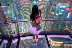 A young woman takes pictures of the city with her mobile phone, from the glass-floor observation platform, in the Oriental Pearl Tower, in the financial district of Shanghai, on May 9, 2019.
