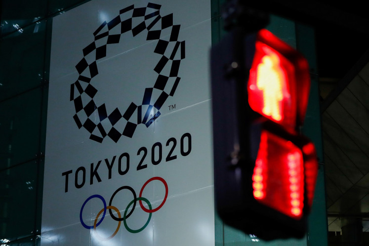 A banner for the upcoming Tokyo 2020 Olympics is seen through a traffic signal in Tokyo, Japan, March 11, 2020. 