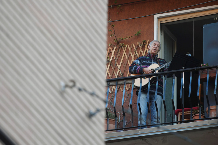 A man plays the guitar and sings from a balcony to raise morale on the sixth day of an unprecedented lockdown across of all Italy imposed to slow the outbreak of coronavirus in Milan, Italy March 15, 2020.  