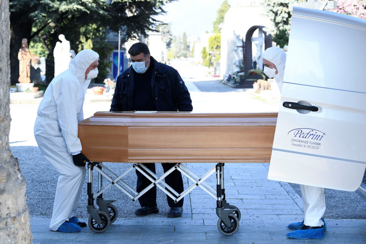 Men in protective masks transport a coffin of a person who died from coronavirus disease (COVID-19), into a cemetery in Bergamo, Italy March 16, 2020. 