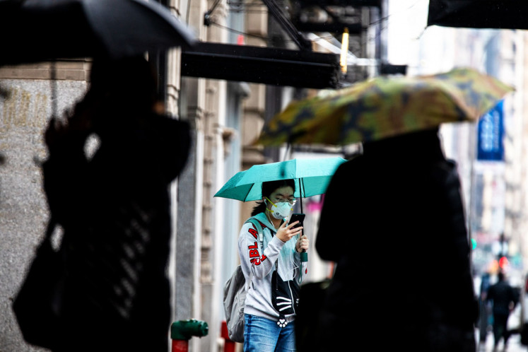 A pedestrian holds an umbrella and her phone while wearing a protective mask in the SoHo neighborhood of New York, U.S., on Tuesday, March 17, 2020. 
