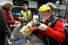 A cashier wearing protective gloves and a welder helmet scans the customers' groceries at a hypermarket in Illiers-Combray, north-west of France, on March 16, 2020, amid the measures taken to contain the spread of COVID-19 due to novel coronavirus. 
