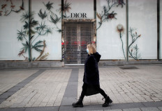 A woman wearing a protective face mask walks past the closed Dior shop on the Champs Elysees Avenue in Paris, France, on March 16, 2020. 