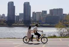 A couple wearing masks to protect against contracting the coronavirus disease (COVID-19) ride on a bicycle at a Han River Park in Seoul, South Korea April 4, 2020. 