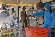 A worker wearing a protective suit sprays disinfectant on bottles in front of a closed shop as a preventive measure against the spread of the COVID-19 coronavirus in Cambodia's Kandal province on April 5, 2020. 