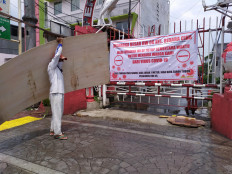 A worker carrying a plywood board passes a banner put up by Bidara Cina residents in East Jakarta on Wednesday. The banner states that the alley of the area where the residents lived is temporarily closed to prevent the spread of Covid-19.