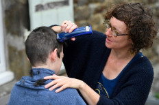 A woman gives her 13-year-old son a haircut outside their home in Hede-Bazouges, Brittany, on April 7, 2020 on the 22nd day of a lockdown in France aimed at curbing the spread of the COVID-19 infection.
