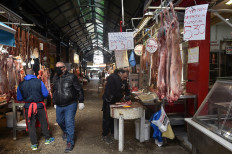 This photograph taken on April 7, 2020, shows a man wearing a protective facemask as he walks past a display of slaughtered sheep at a meat market in Thessaloniki. 