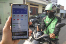 A customer holds up their mobile phone in Kalisari, East Jakarta, on Friday to show the home screen of the Gojek app, which is missing the Go-ride feature. For the next two weeks and as part of Jakarta's large-scale social restriction measures, motorcycle taxi drivers from Gojek and Grab will not be allowed to transport passengers, only packages and food.