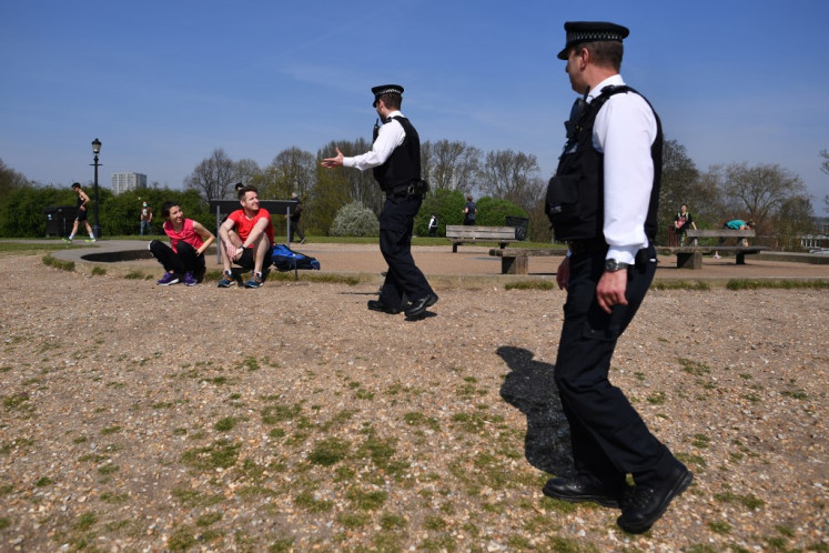 Police officers talk with a couple resting on Primrose Hill in London on April 10, 2020 as warm weather tests the nationwide lockdown and the long Easter weekend begins. - The disease has struck at the heart of the British government, infected more than 60,000 people nationwide and killed over 7,000, with another record daily death toll of 881 reported on April 9. 