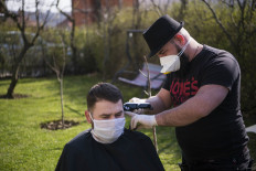 Kosovo hairdresser Driton Kameri (R) wears a facemask as he cuts the hair of a client in his garden on March 30, 2020 in Pristina during the time of COVID-19 pandemic. 