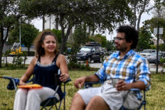 Italian chef Aldo Giaquinto (right) and his wife Vera Kozlovskaia eat their breakfast in a park near a Walmart parking lot where they are living out of their car in Miami, on April 10, 2020. - The couple has lived for the past two weeks camped out in their converted Toyota Land Cruiser in a Walmart parking lot. 