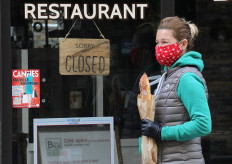 A woman wearing a protective face mask holds a French baguette as she walks past a closed restaurant in Cannes during a lockdown imposed to slow the rate of the coronavirus disease (COVID-19) in France, April 16, 2020. 