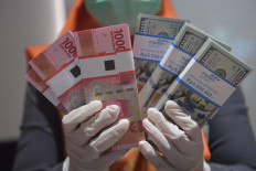An employee holds up wads of rupiah and United States dollar notes at Bank Mandiri Syariah in Jakarta on April 20, 2020.