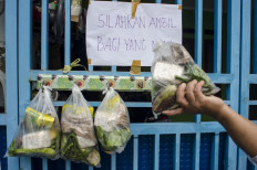 A resident takes a food package offered by Dwi Fitria Ambarina in Cimahi, West Java, on Wednesday. Dwi hung more than a dozen bags of food on the gate of her home to help neighbors affected by COVID-19.
