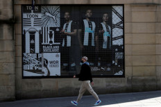 A man wearing a protective face mask passes near an advertisement of the Newcastle United Football Club, as the spread of the COVID-19 continues, in Newcastle, Britain, April 25, 2020. A bid by a Saudi Arabian state fund to secure ownership of Newcastle United is drawing scrutiny, but even if it succeeds it is unlikely that the petrodollars will transform the Premier League club into a powerhouse in the near future.