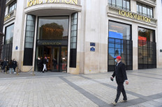 A man wearing a mask walks past clients queueing to enter Louis Vuitton shop on the Champs-Elyees avenue in Paris on May 11, 2020 on the first day of France's easing of lockdown measures in place for 55 days to curb the spread of the COVID-19 pandemic, caused by the novel coronavirus.
