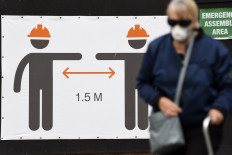 A woman wearing a face mask walks before a sign promoting social distancing measures in Sydney on May 13, 2020. - 