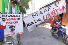 A couple on motorcycle drive past a makeshift gate in a residential area in Citeureup, Bogor, West Java, on May 7. The gate displays a banner declaring a “lovedown” instead of a lockdown. JP/P.J. Leo