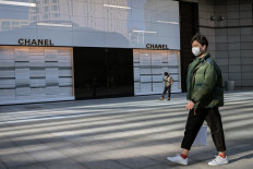 A man (right) wearing a face mask amid the COVID-19 coronavirus outbreak walks past a Chanel shop in Beijing on April 2, 2020.