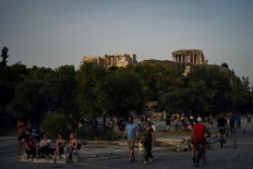 People walk with in background the ancient Temple of Parthenon atop the Acropolis hill in Athens on May 17, 2020 during the gradual deconfinement started on May 4, following a lockdown aimed at curbing the spread of the COVID-19 pandemic, caused by the novel coronavirus. 