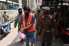 A man wears a mandatory orange vest while picking up trash in Tanah Abang, Central Jakarta, as punishment for violating large-scale social restrictions on May 13.