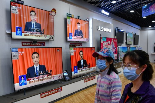 People walk past televisions broadcasting live coverage from Beijing of Chinese Premier Li Keqiang delivering his speech during the opening session of the National People's Congress (NPC), at a shopping mall in Yantai in China's eastern Shandong province on May 22, 2020. 