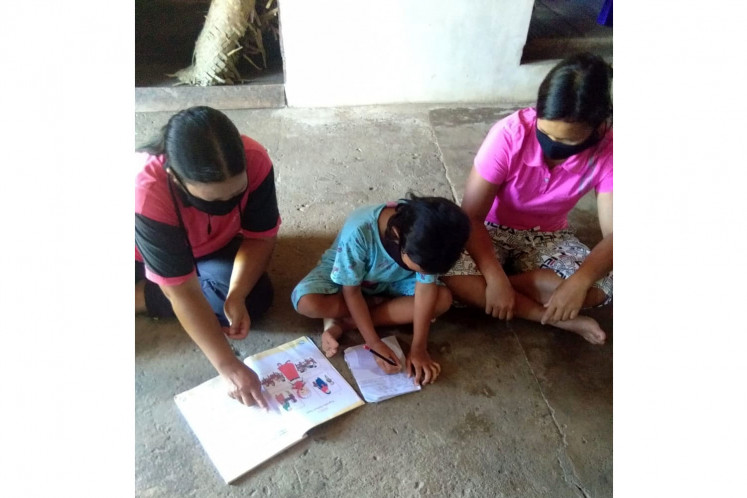 Wearing mask, Yuliana (right), a teacher at SD 08 state elementary school in Berinang Mayung in Landak regency, West Kalimantan, teaches a student (center) who is accompanied by her parent.