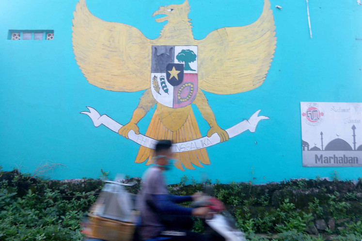 A motorcyclist passes a Garuda Pancasila mural painted on a wall on Jl. Puspitek Raya in South Tangerang, Banten.
