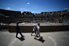 Visitors (center) followed by a member of security staff, walk across the Colosseum monument which reopens to the public on June 1, 2020 in Rome, while the country eases its lockdown aimed at curbing the spread of the COVID-19 infection, caused by the novel coronavirus.