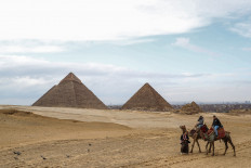 A camel guide leads tourists on camels at the Giza pyramids plateau overlooking the Giza necropolis on the southwestern outskirts of the Egyptian capital on March 13, 2020, as in the background are seen the Pyramid of Khafre (Chephren) and Menkaure (Menkheres).
