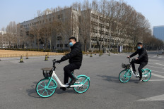 Two men wear face masks as a preventive measure against the COVID-19 coronavirus as they ride bikes in the empty grounds of Tsinghua University in Beijing on February 28, 2020. 