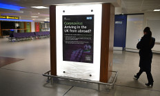 A woman passes an advert alerting passengers arriving into the UK, about the government's advice on COVID-19, at almost-empty departure hall at Terminal 1 of Manchester Airport in Manchester, northern England on May 11, 2020, where they have begun a trial of body temperature screening during the COVID-19 pandemic. 