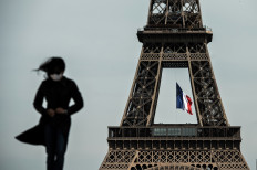 In this file photo taken on May 11, 2020 a woman wearing a face mask walks as a French national flag flies on the Eiffel Tower in background in Paris on the first day of France's easing of lockdown measures in place for 55 days to curb the spread of the COVID-19 pandemic, caused by the novel coronavirus. 