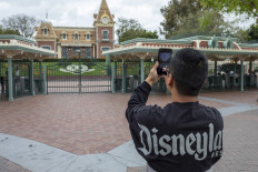In this file photo taken on March 14, 2020 a man takes a photo outside the gates of Disneyland Park on the first day of the closure of Disneyland and Disney California Adventure theme parks as fear of the spread of coronavirus continue, in Anaheim, California. 