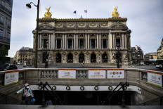 A man wearing a facemask walks up steps out of a metro station in front of the Opera Garnier in Paris on April 21, 2020.