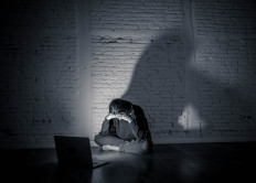 A young woman weeps in front of a computer in this photo to illustrate cyberbullying. 