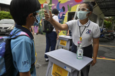A staff member checks the temperature of a student on the first day of the reopening of the International Pioneers School in Bangkok on June 16, 2020, following its temporary closure due to the COVID-19 coronavirus epidemic. - Some schools in Thailand have reopened as they adopted preventive measures such as social distancing and regular disinfection to halt the spread of the virus. 