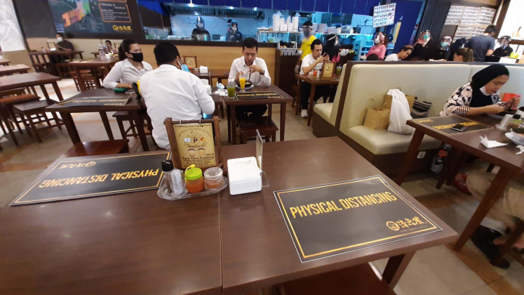 Play it safe: People eat at a restaurant in Jakarta on Monday. Due to the COVID-19 pandemic, restaurants have placed physical distancing signs on tables. Since viruses like the novel coronavirus are contagious, maintaining a safe distance is urged in public places.